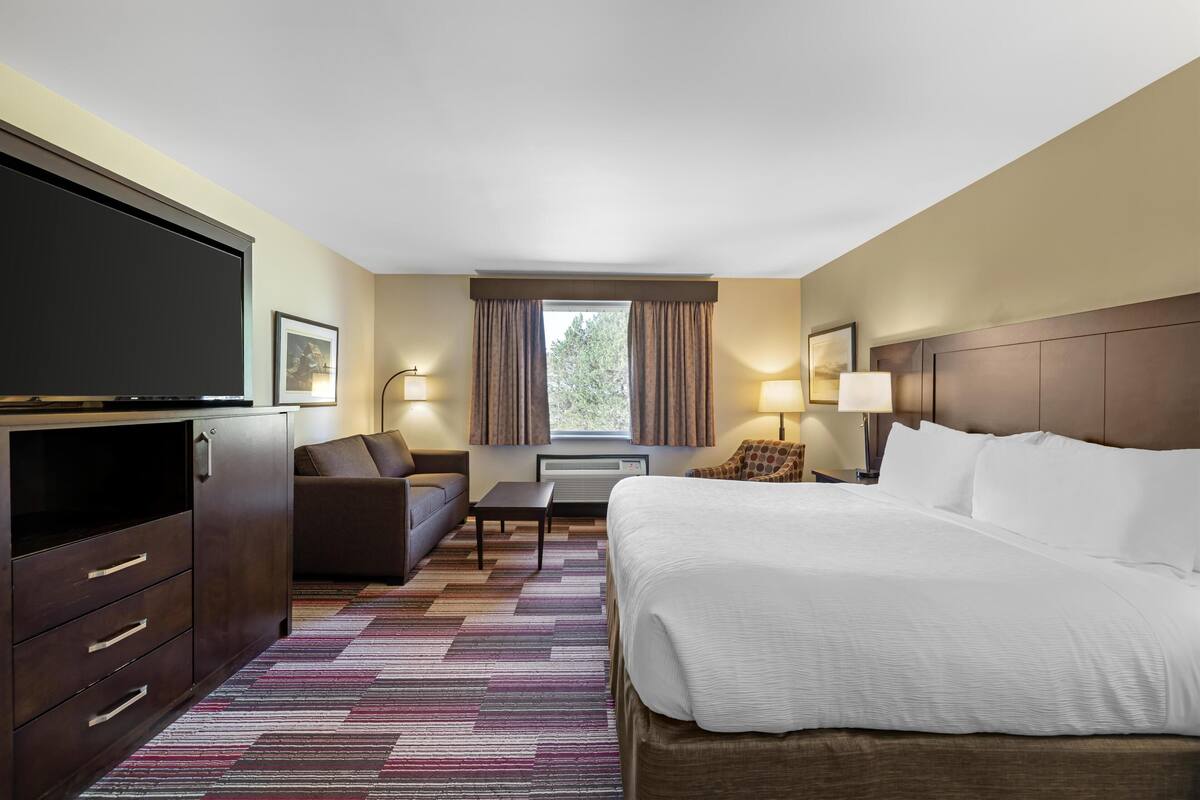 A hotel room with a bed, a TV, a sofa, a coffee table, and a window with curtains.