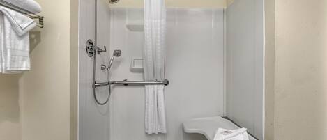 A shower with a glass door, a white shower curtain, and a handheld showerhead.