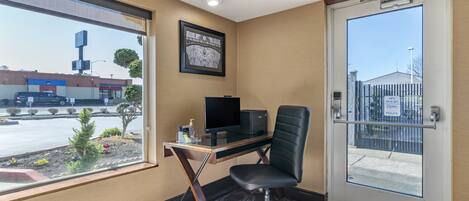 A hotel room with a desk, chair, and a large window offering a view of the street and a building.