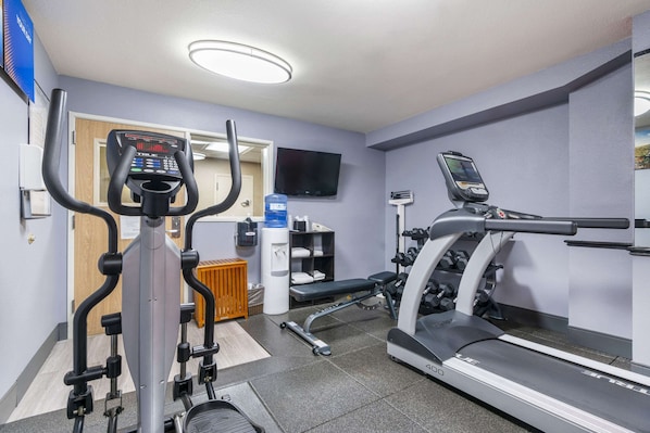Un gimnasio con cinta de correr, elíptica y banco para pesas.