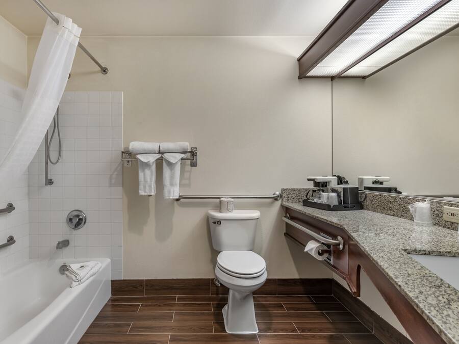 Uma casa de banho moderna com sanita branca, banheira com cortina de chuveiro, toucador com bancada e porta-toalhas.