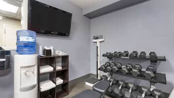 Un gimnasio con dispensador de agua, una banca y mancuernas en estanterías.