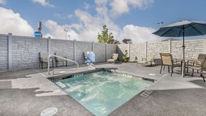 An outdoor swimming pool with lounge chairs and an umbrella, surrounded by stone walls and a clear sky. - Comfort Inn Troutdale - Portland East (Troutdale)