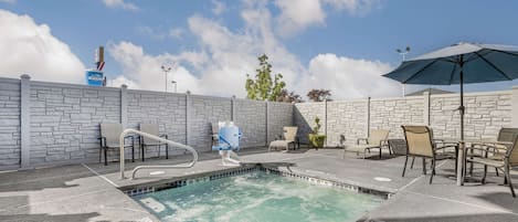 An outdoor swimming pool with lounge chairs and an umbrella, surrounded by stone walls and a clear sky.