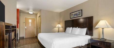 A hotel room with a large bed, two bedside lamps, a wooden headboard, a desk with a lamp, and a wardrobe.
