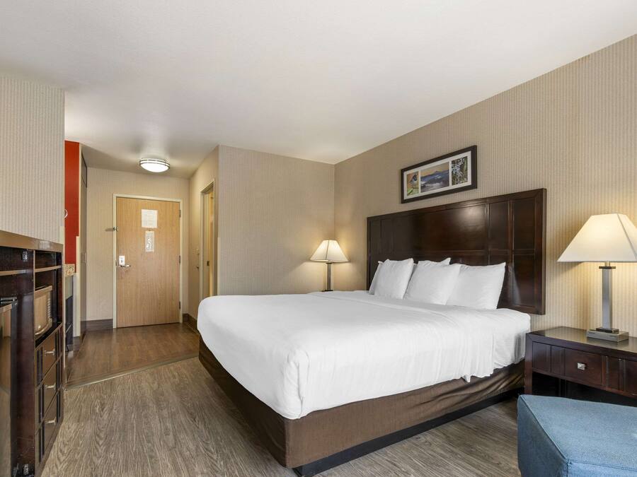 A hotel room with a large bed, two bedside lamps, a wooden headboard, a desk with a lamp, and a wardrobe.