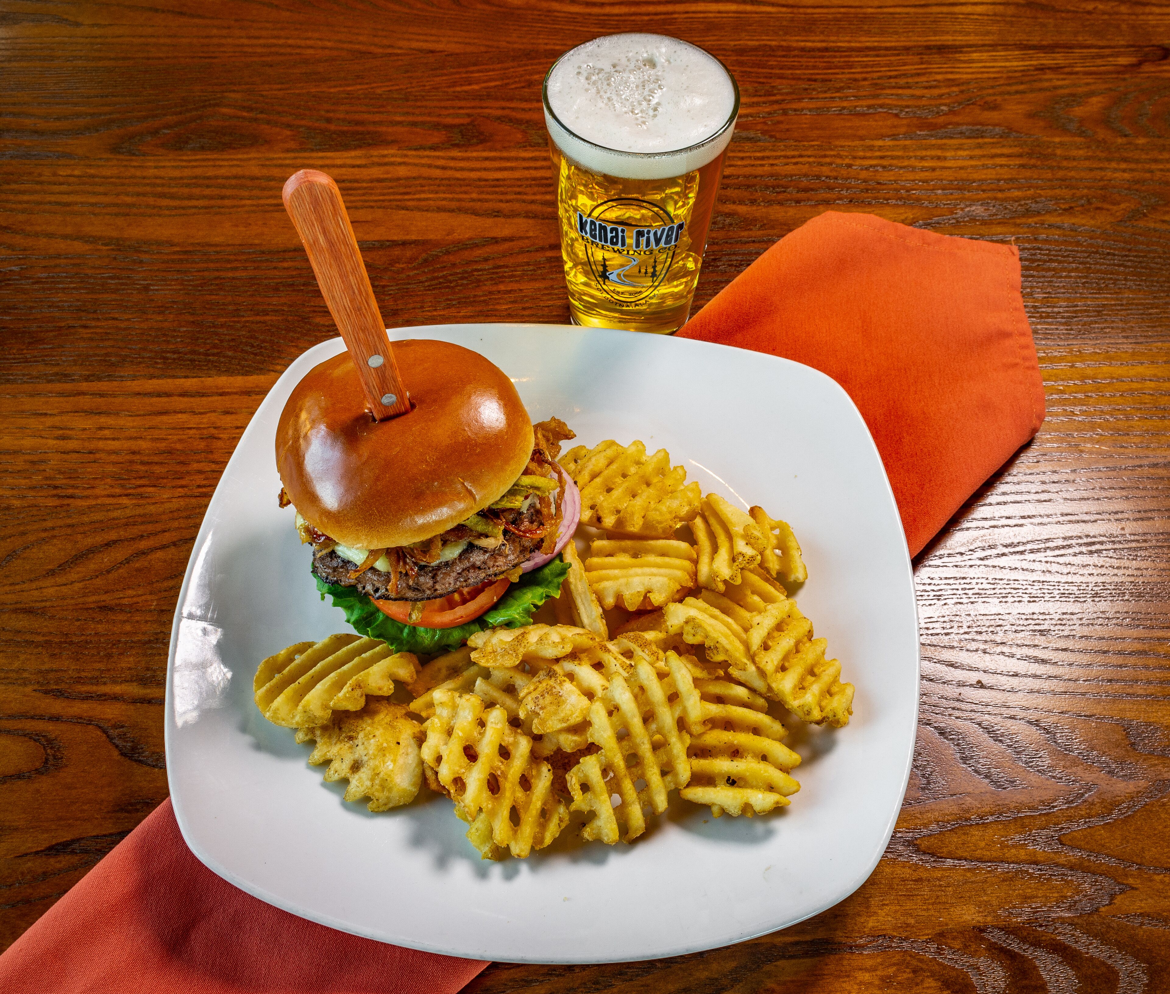 A plate with a burger and fries, a beer glass, and a wooden table.