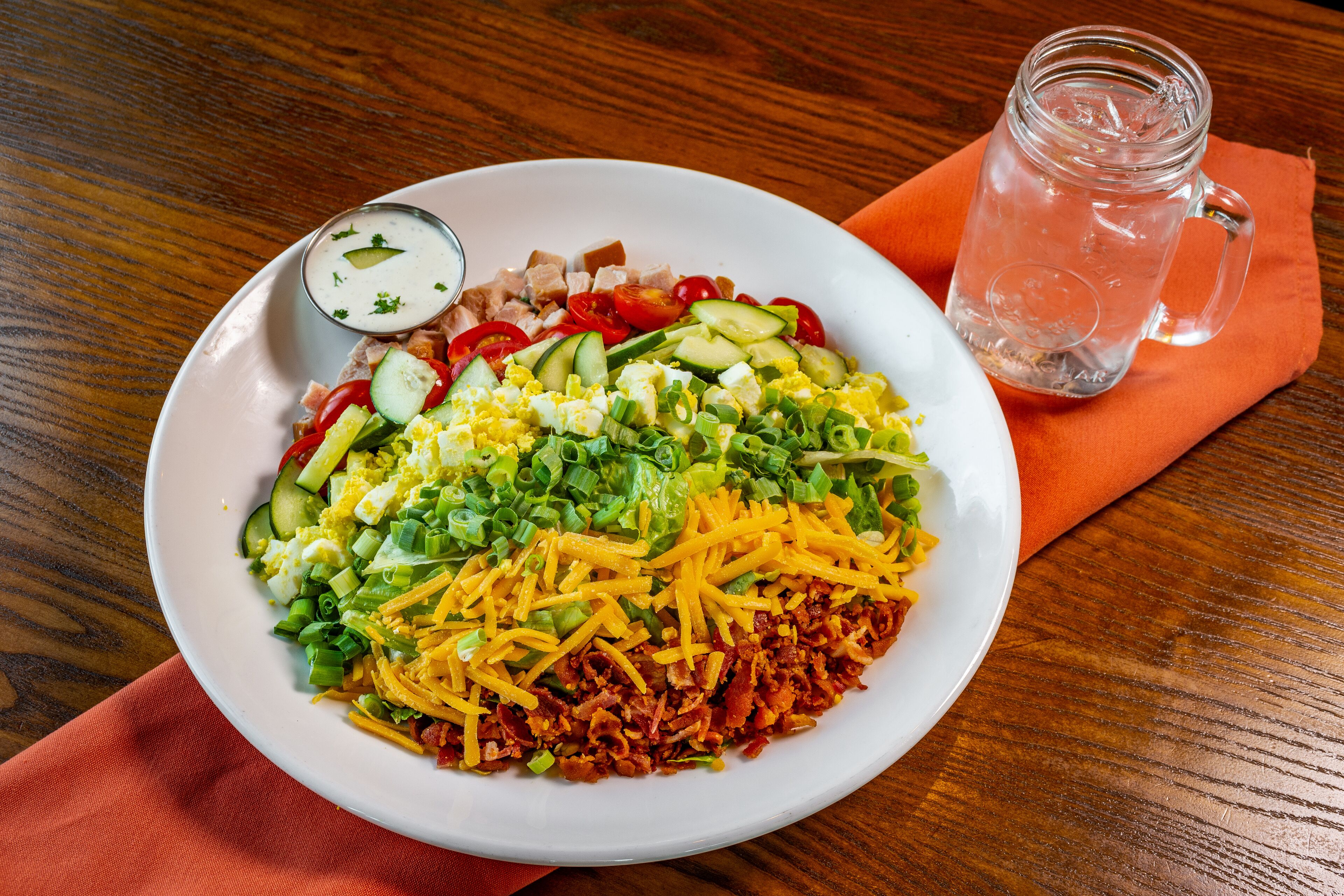 A plate of food with various toppings and a small bowl of sauce, placed on a wooden table with a glass of iced tea.
