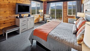 A wooden cabin room with a bed, a TV, a desk, and a chair.