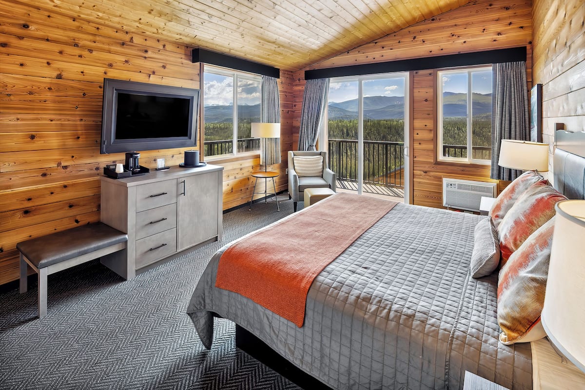 A wooden cabin room with a bed, a TV, a desk, and a chair.