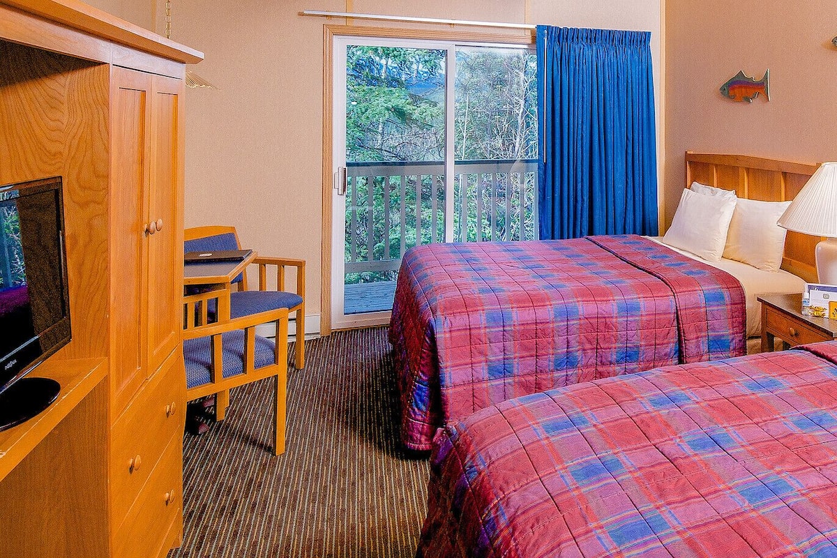 A hotel room with two beds, a TV, a desk, and a window with curtains.