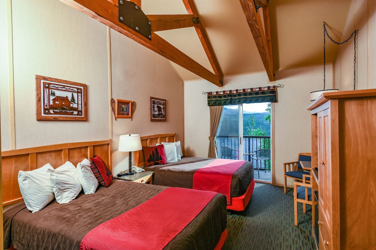A hotel room with two beds, wooden headboard, a balcony with a view, and a wooden wardrobe.