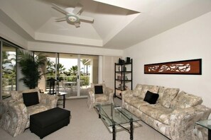 A modern living room with a ceiling fan, two sofas, a glass coffee table, and a bookshelf. - Vista Waikoloa (Waikoloa)