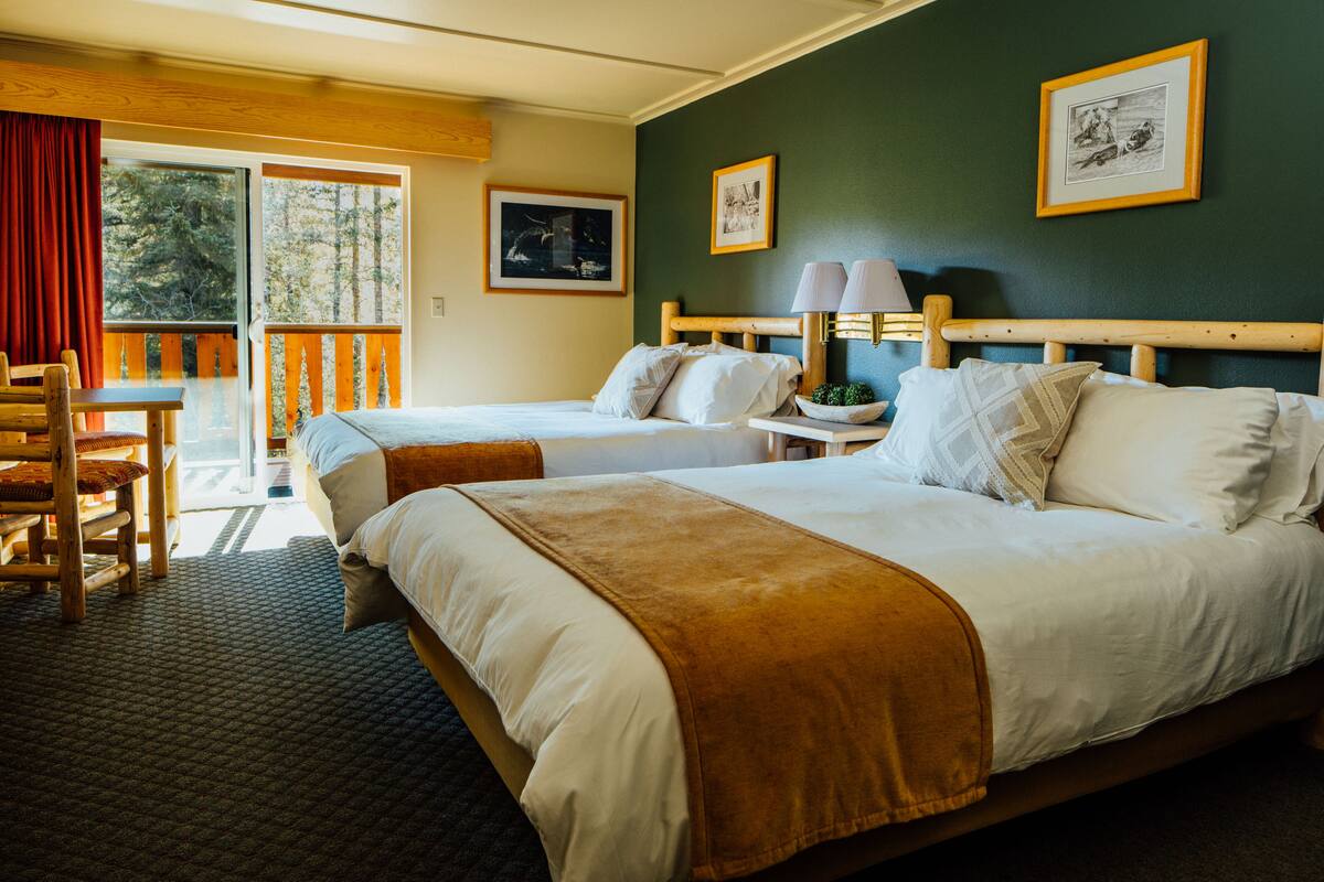Habitación de hotel con dos camas, cabecera de madera, una mesita y una silla.
