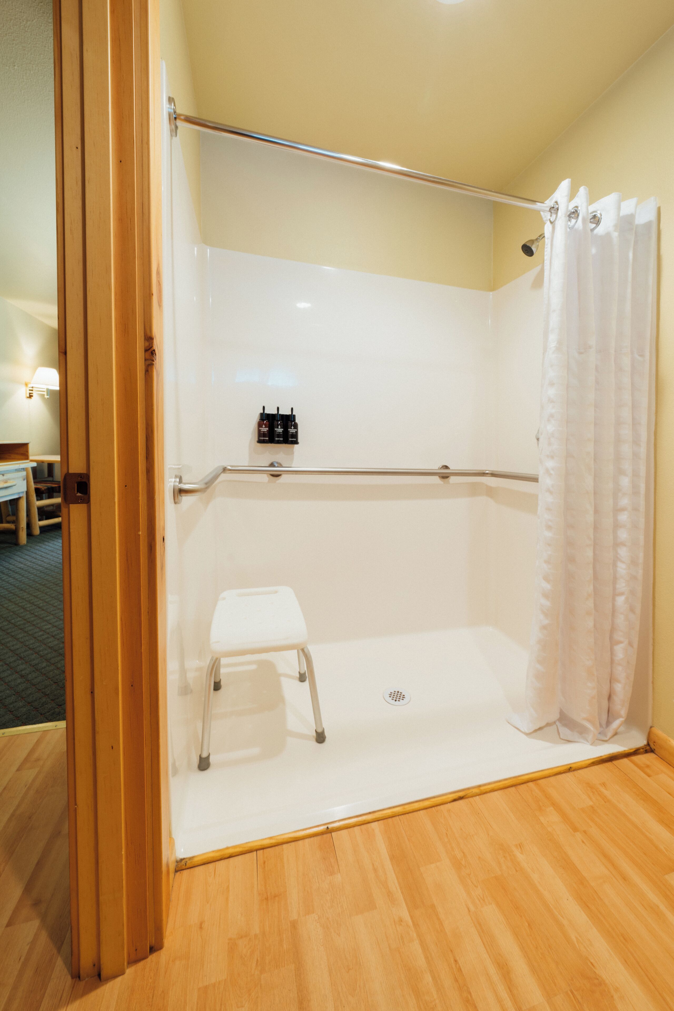 Une douche avec un petit marchepied blanc, un rideau de douche et une étagère avec des bouteilles.