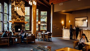 A cozy interior with a stone fireplace, wooden furniture, and large windows offering views of the outdoors. - Seward Windsong Lodge (Seward)