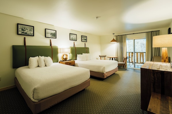 A hotel room with two beds, a small table, a chair, and a balcony with curtains. - Seward Windsong Lodge (Seward)