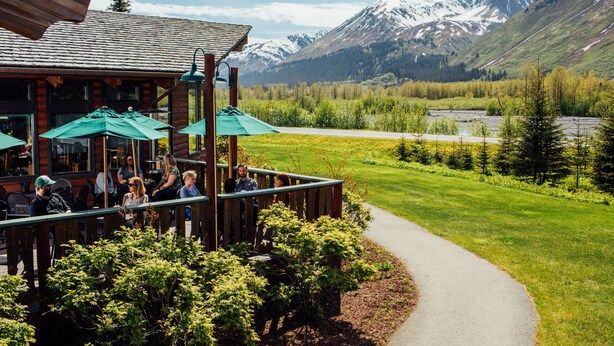 A wooden building with outdoor seating and a view of a mountain range. - Seward Windsong Lodge (Seward)
