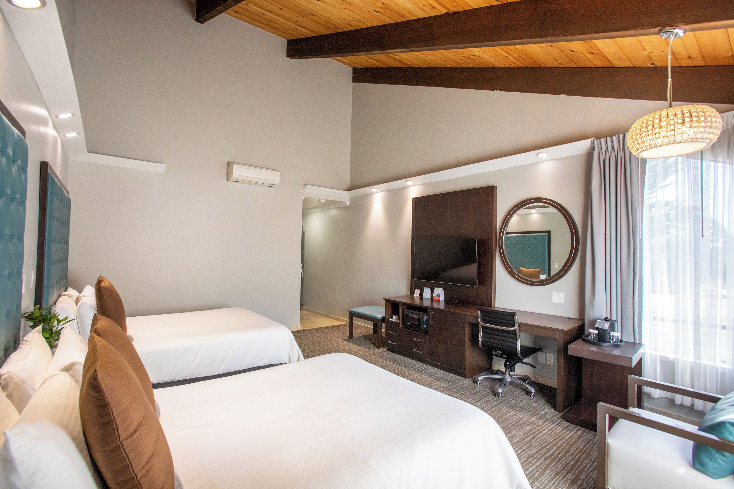 A hotel room with two beds, a desk, a television, and a large mirror.