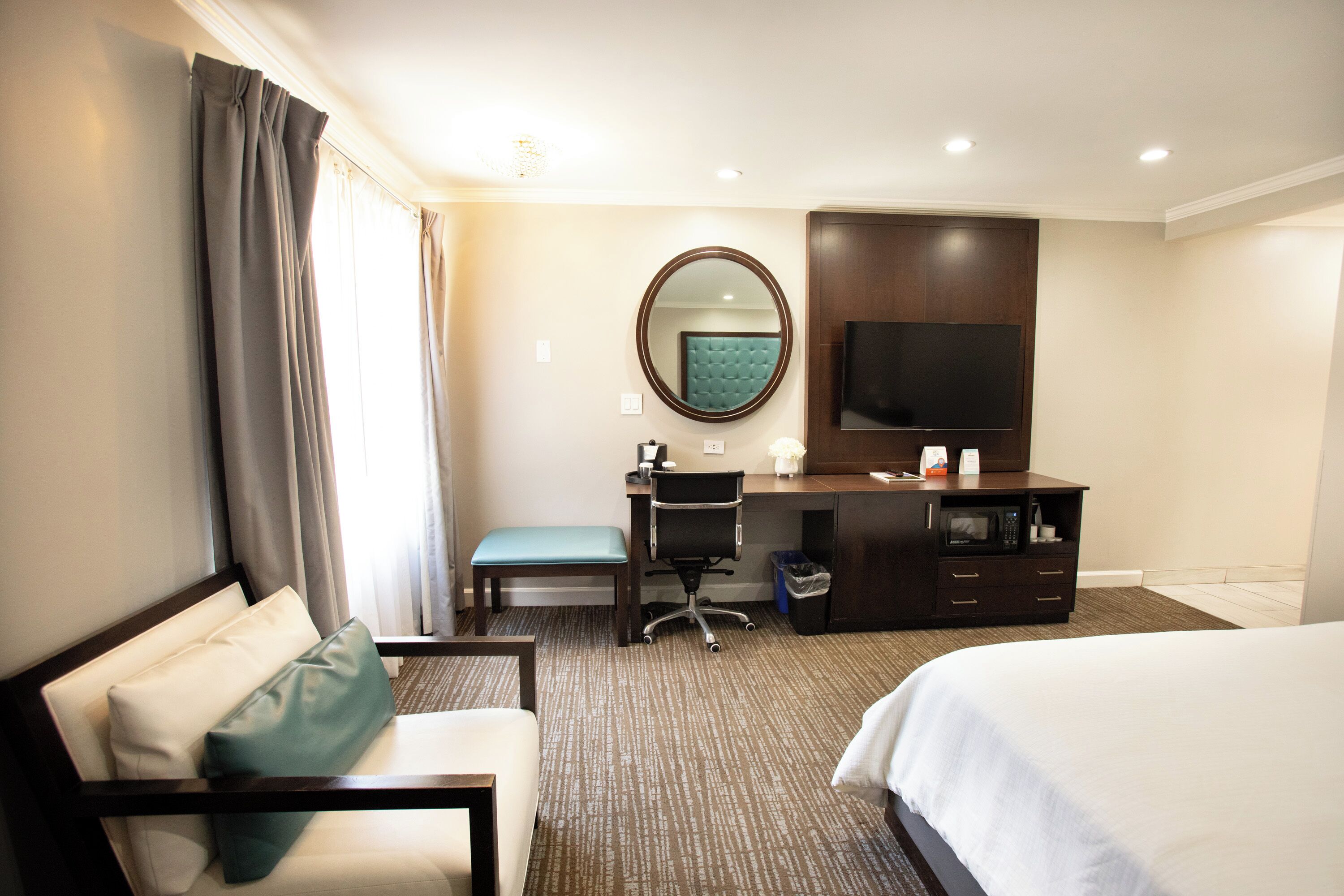 Habitación de hotel con cama, escritorio con silla, televisión, espejo y ventana con cortinas.