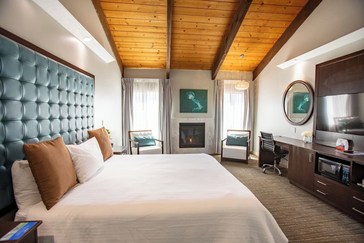 A hotel room with a large bed, a desk, a chair, a television, and a fireplace.
