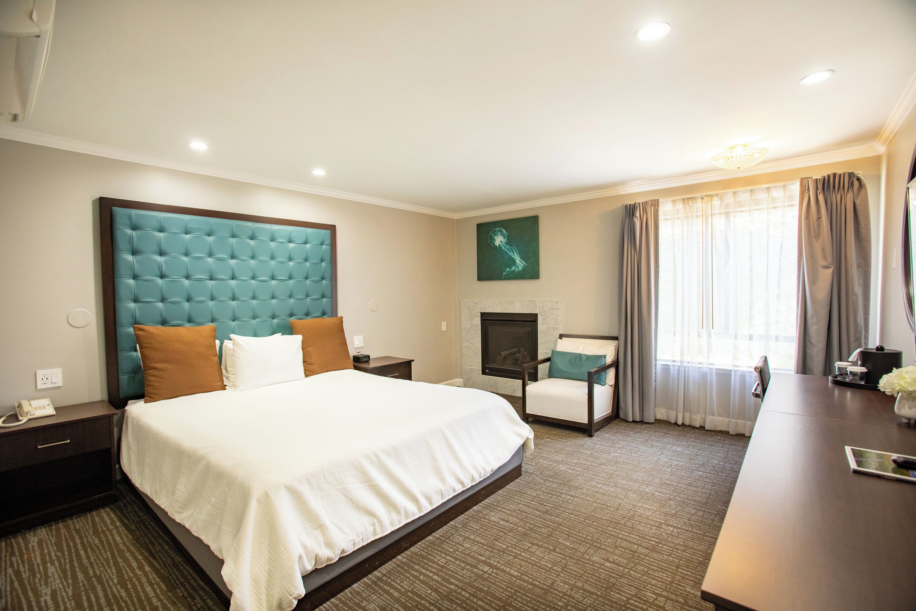 A hotel room with a large bed, a desk, a chair, a fireplace, and a large window with curtains.