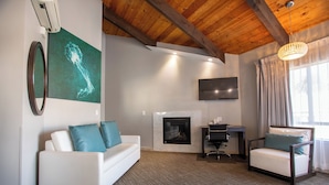 Una sala de estar moderna con un sofá blanco, una butaca, una chimenea, un televisor de pantalla plana y techo de madera.