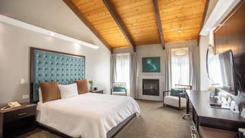 A hotel room with a large bed, a desk, a fireplace, and a television.