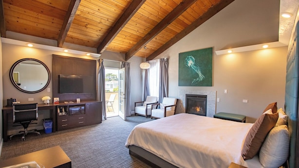 Habitación de hotel con techo de madera, una cama grande, un escritorio con teléfono, una silla, una chimenea y un cuadro en la pared.