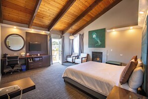 Habitación de hotel con techo de madera, una cama grande, un escritorio con teléfono, una silla, una chimenea y un cuadro en la pared.