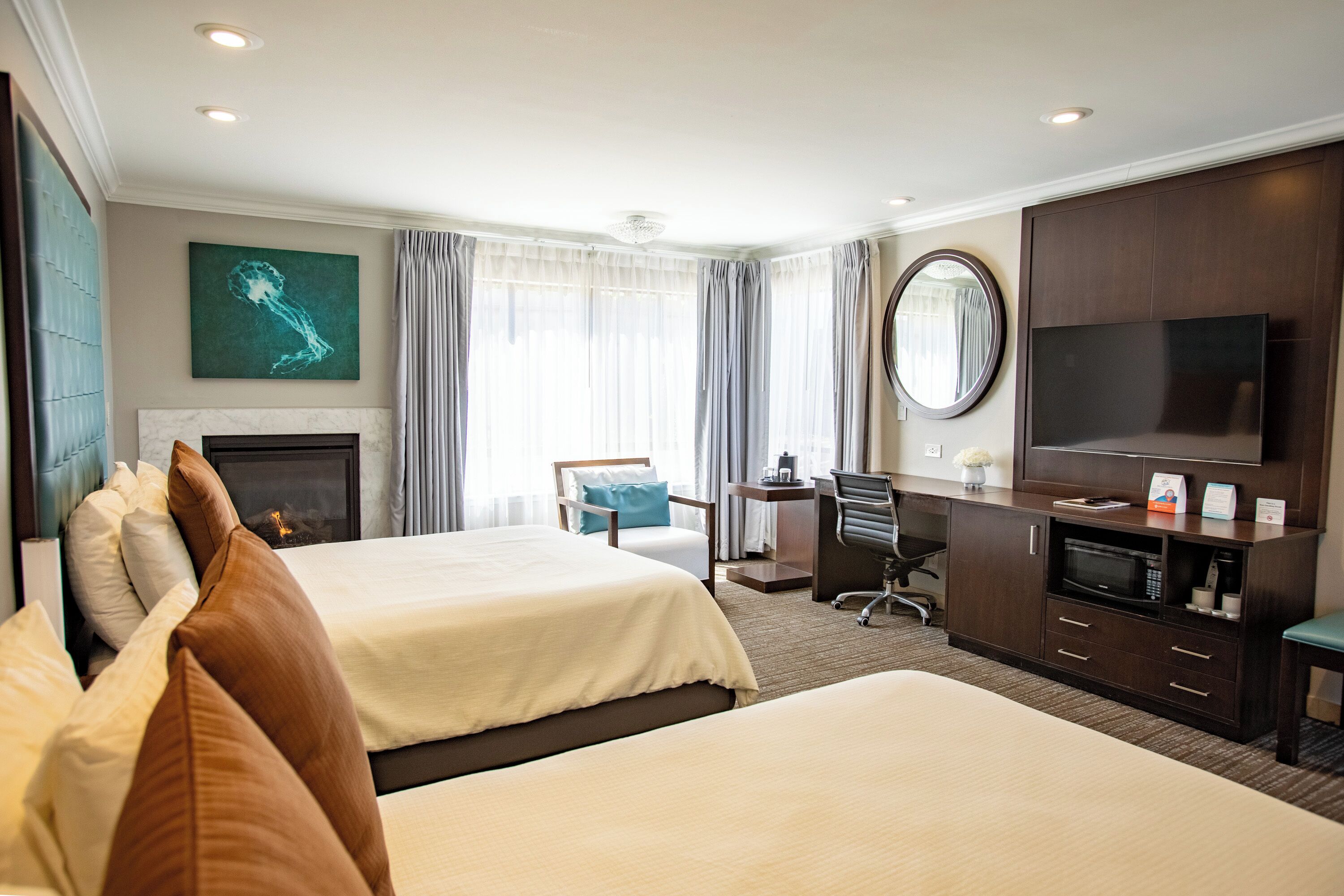 Habitación de hotel con dos camas, un escritorio, un televisor, una chimenea y un espejo grande.
