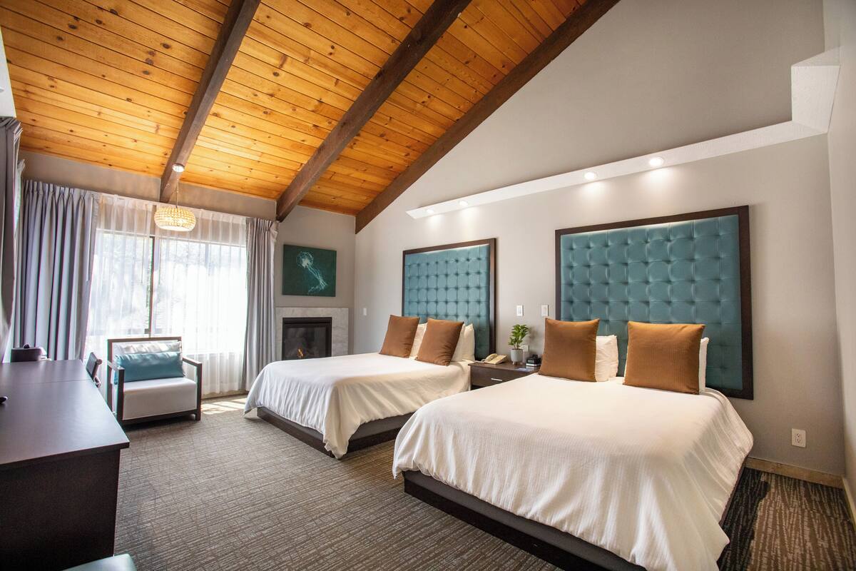 A hotel room with two beds, a desk, a chair, and a large window with curtains.