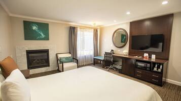 A hotel room with a large bed, a desk with a chair, a television, a fireplace, and a large mirror.