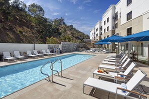 A pool area with lounge chairs and umbrellas, surrounded by a building with a view of a hillside. - Homewood Suites by Hilton San Diego Hotel Circle/SeaWorld Area (San Diego)