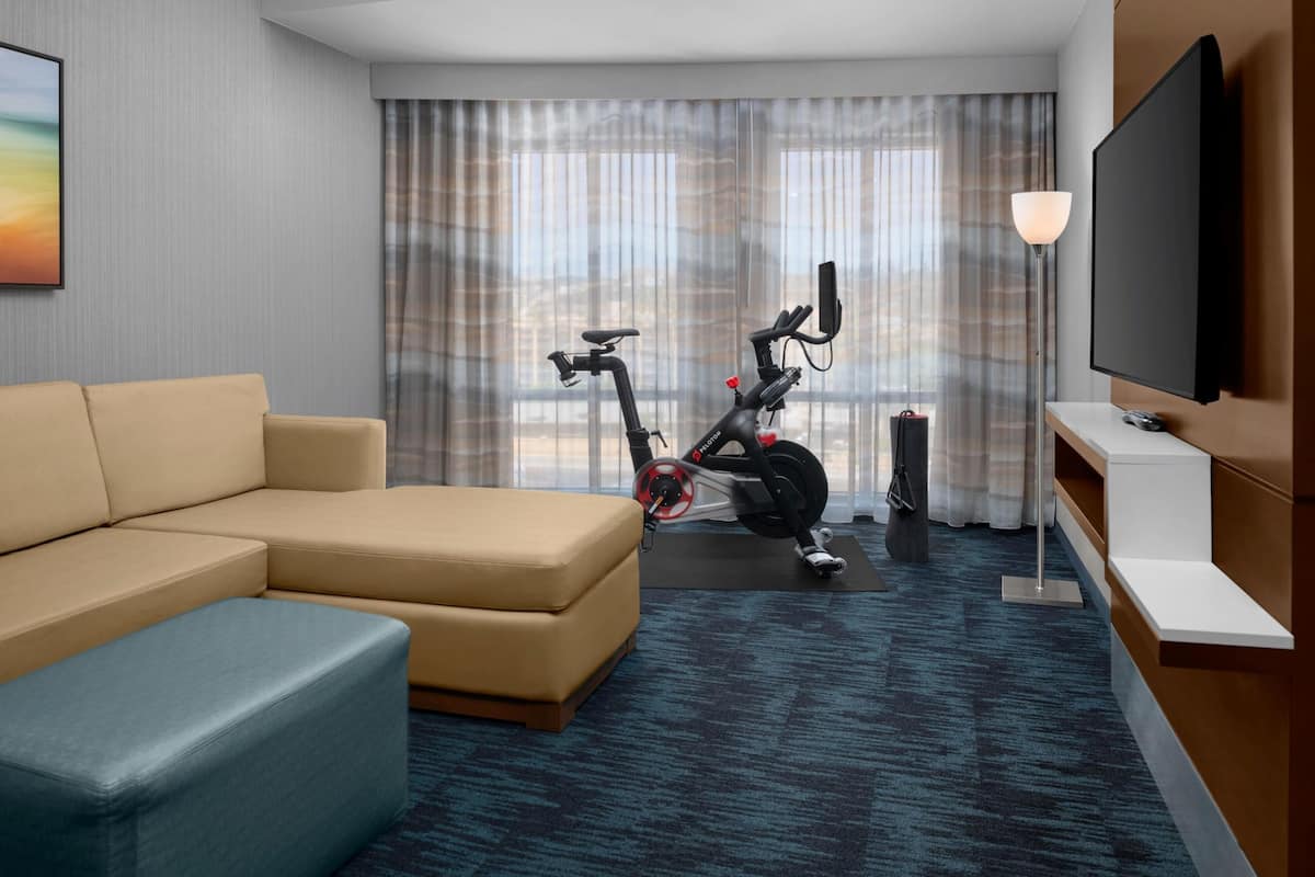 Habitación de hotel con sofá, bicicleta estática, televisión y vistas al exterior.