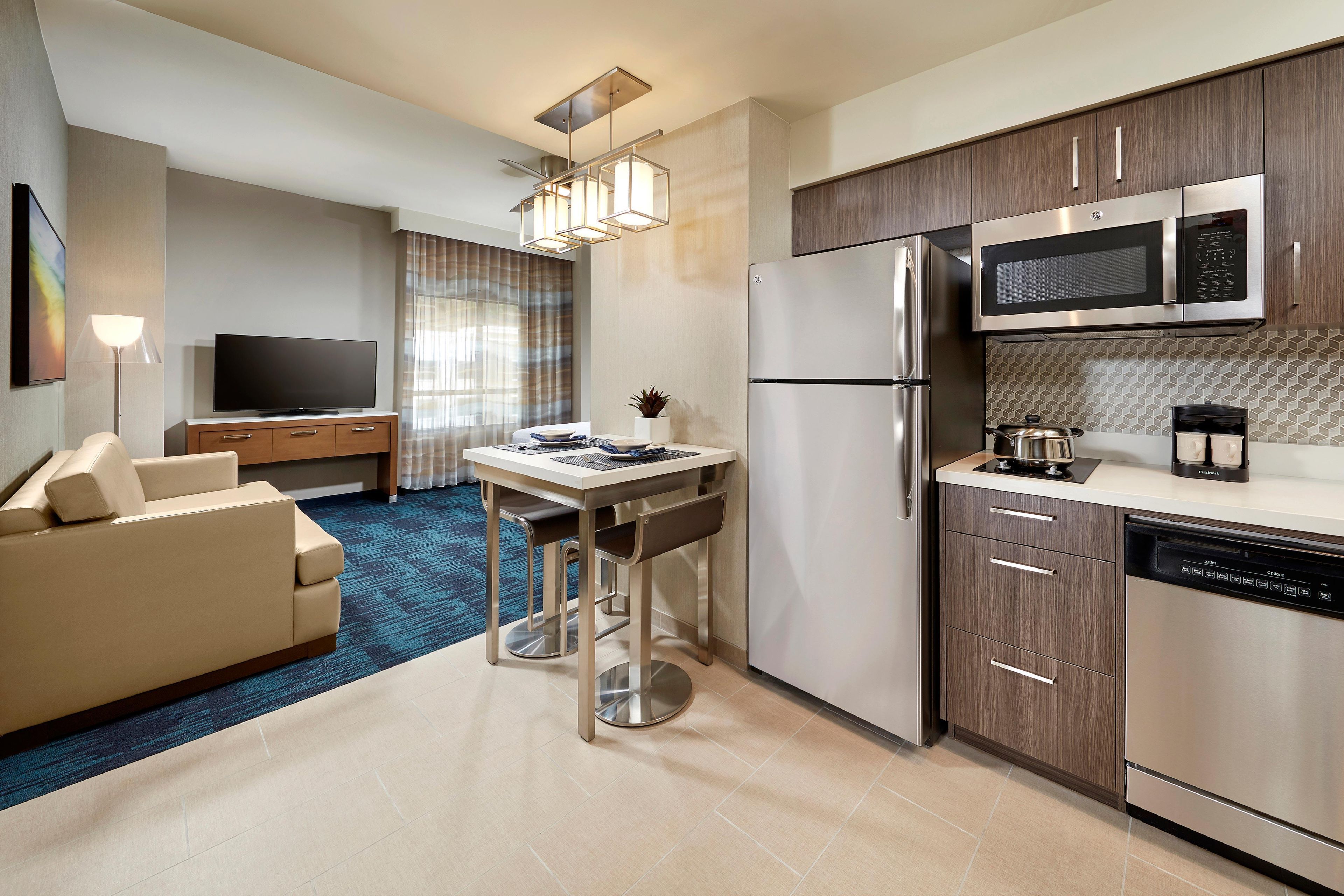 A modern kitchen with stainless steel appliances, a dining area with a table and chairs, and a living area with a sofa and TV.