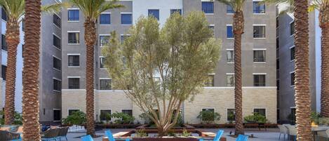 A courtyard with palm trees, blue chairs, and a building with multiple windows.