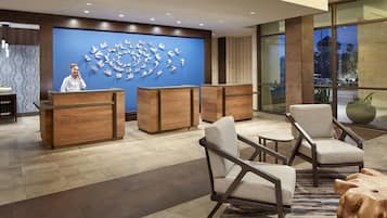 A hotel reception area with a receptionist, wooden reception desks, and a large wall art installation.