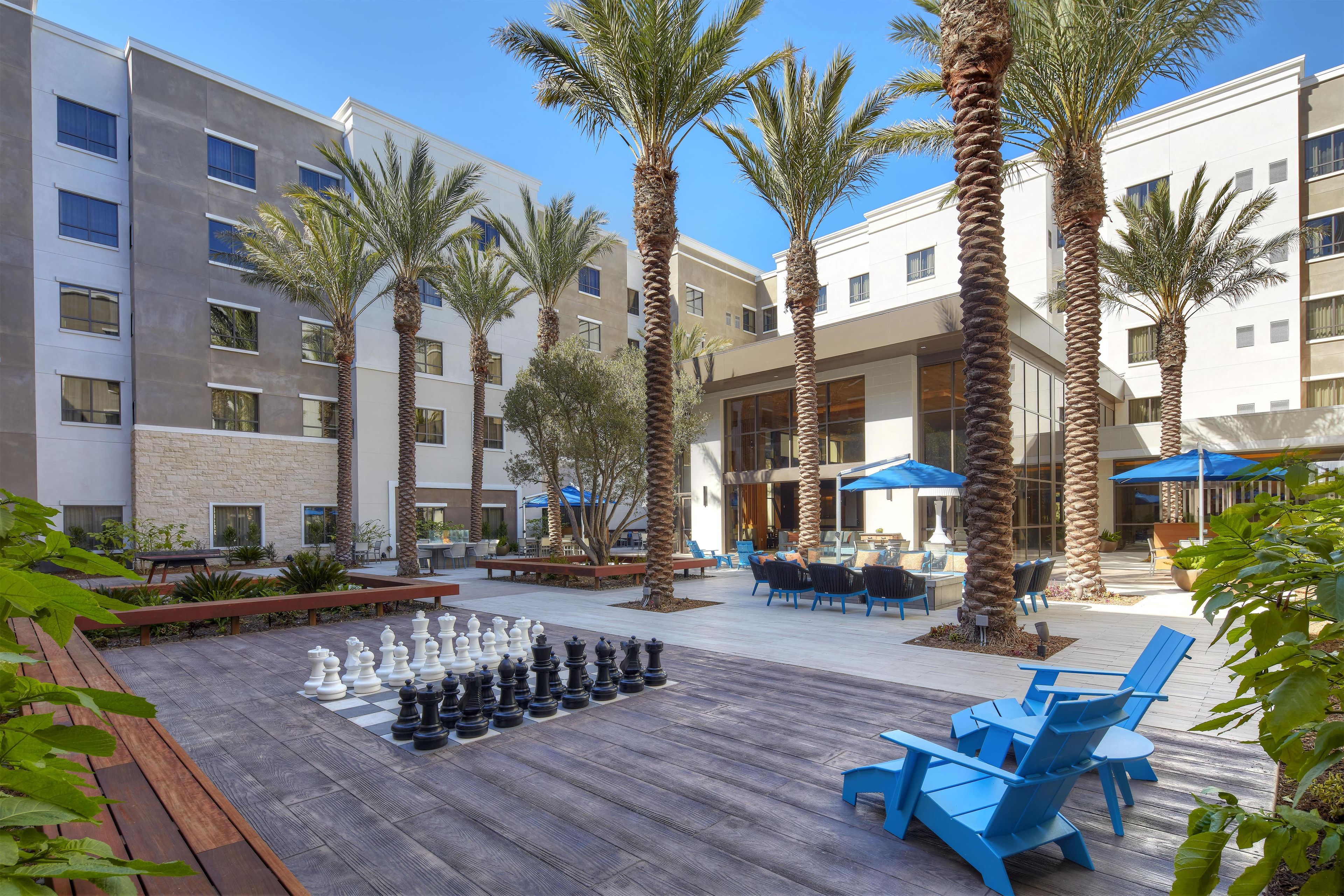 A courtyard with outdoor seating, palm trees, and a chessboard.