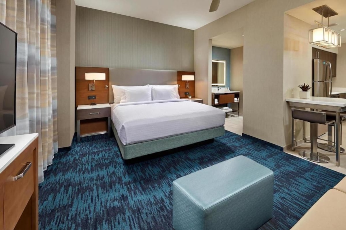 Una habitación de hotel con una cama grande, un escritorio con silla, un baño y un pequeño rincón de estar.
