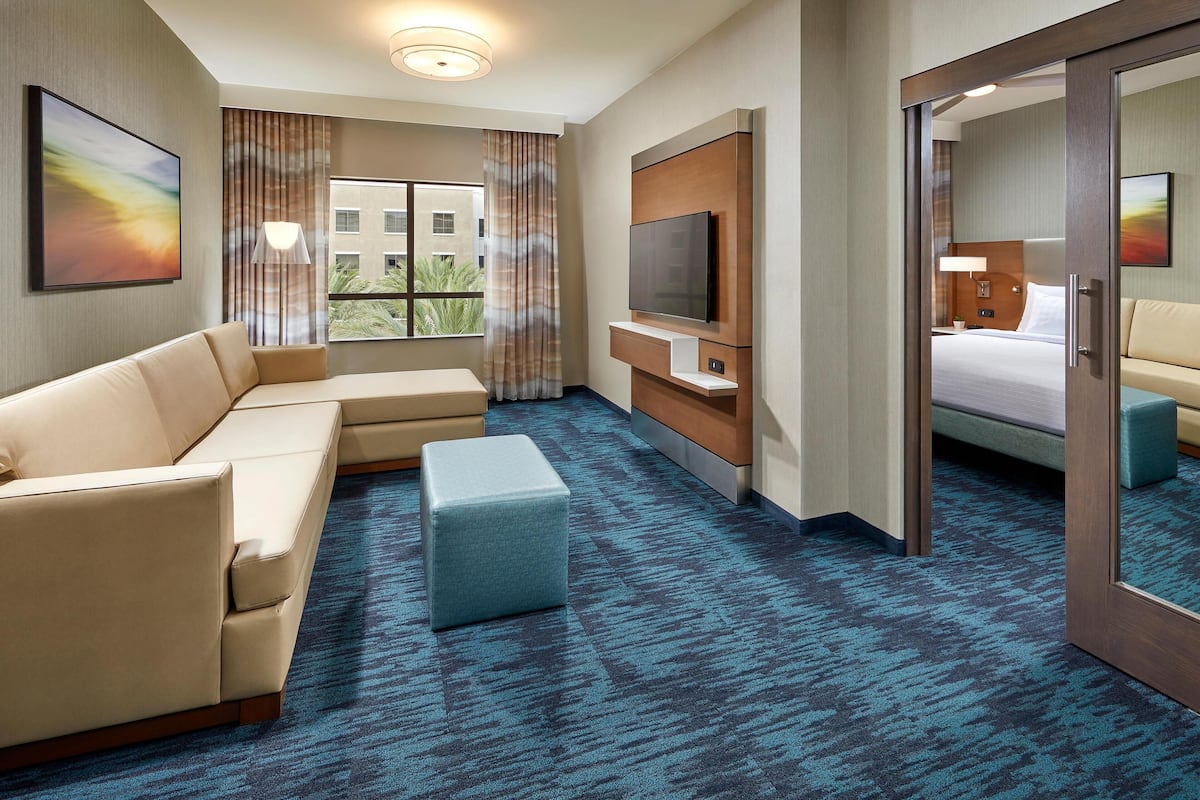 Habitación de hotel con sofá, reposapiés, televisor y cama con vistas a edificios.