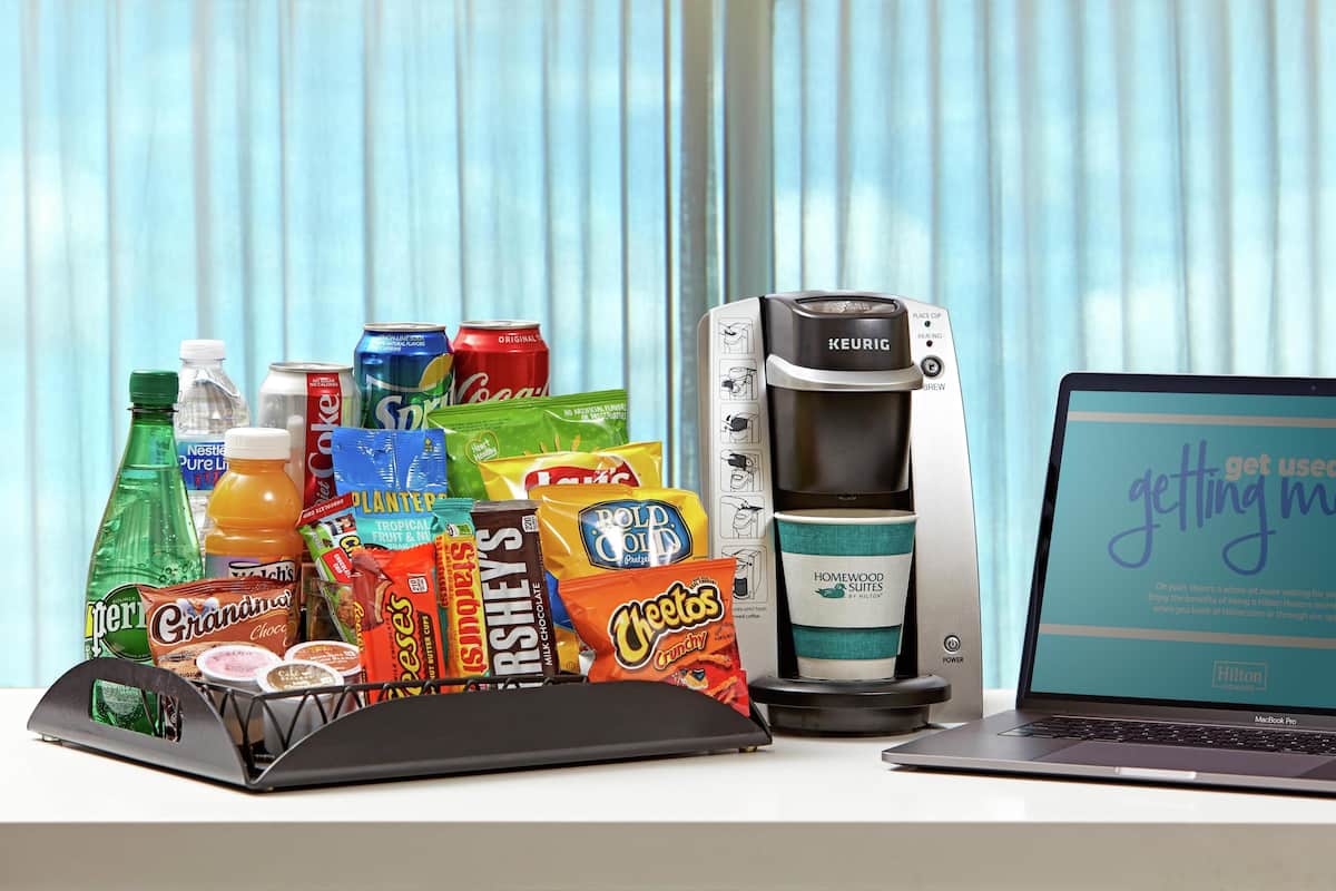 Una kitchenette con una cafetera Keurig, una laptop y diferentes bocadillos.