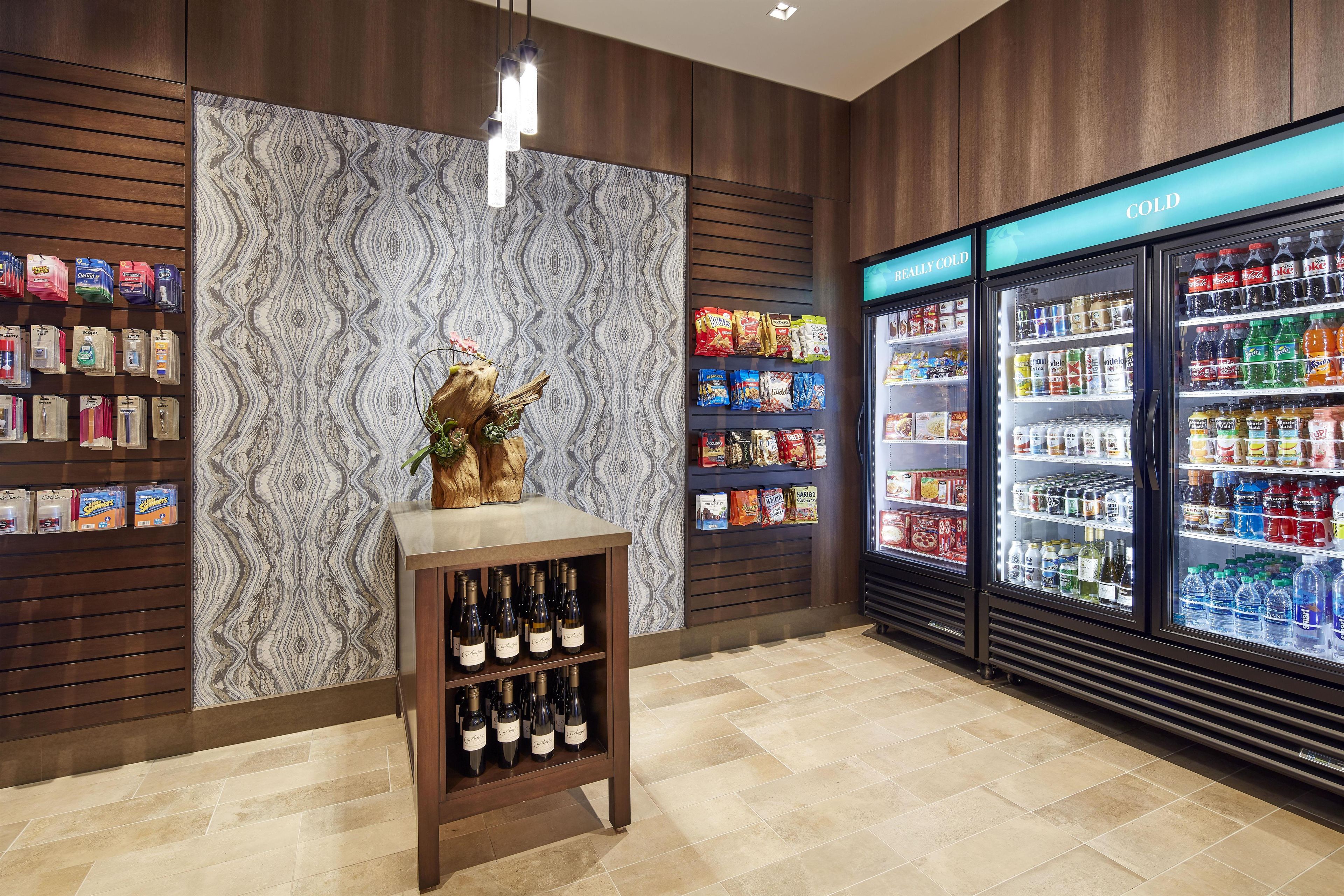 A retail store interior with a wine cooler, snack shelves, and a decorative wooden stand.