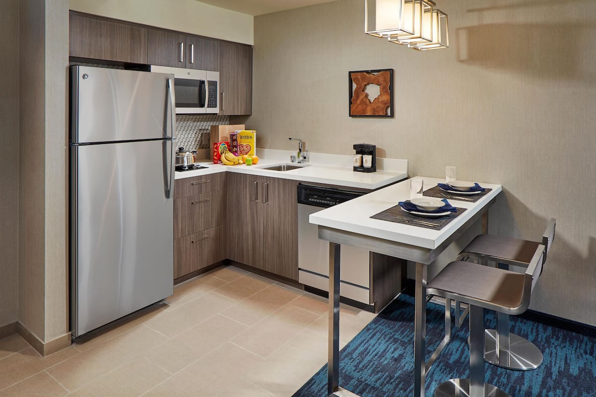 Una cocina moderna con un refrigerador de acero inoxidable, microondas y lavavajillas. Hay un pequeño comedor con una mesa y sillas.