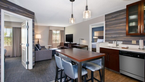 A modern hotel room with a dining area, a kitchen with a dishwasher, and a seating area with a TV and lamp. - Residence Inn by Marriott Ann Arbor North (Ann Arbor)