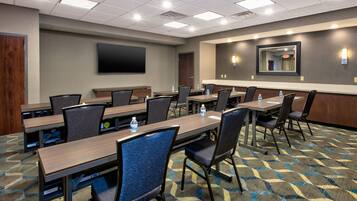A conference room with multiple tables and chairs, a flat-screen TV, and a large mirror on the wall.