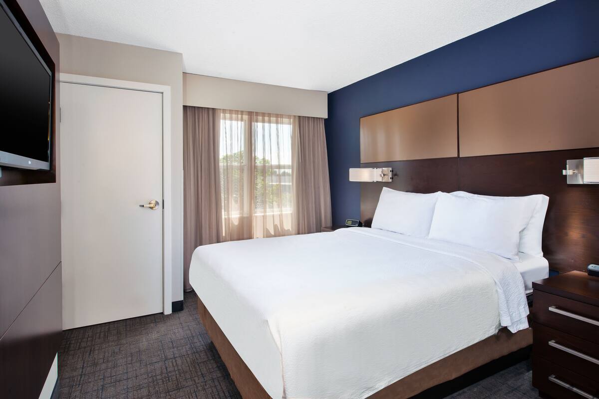 A hotel room with a large bed, a TV mounted on the wall, a bedside table, and a door.