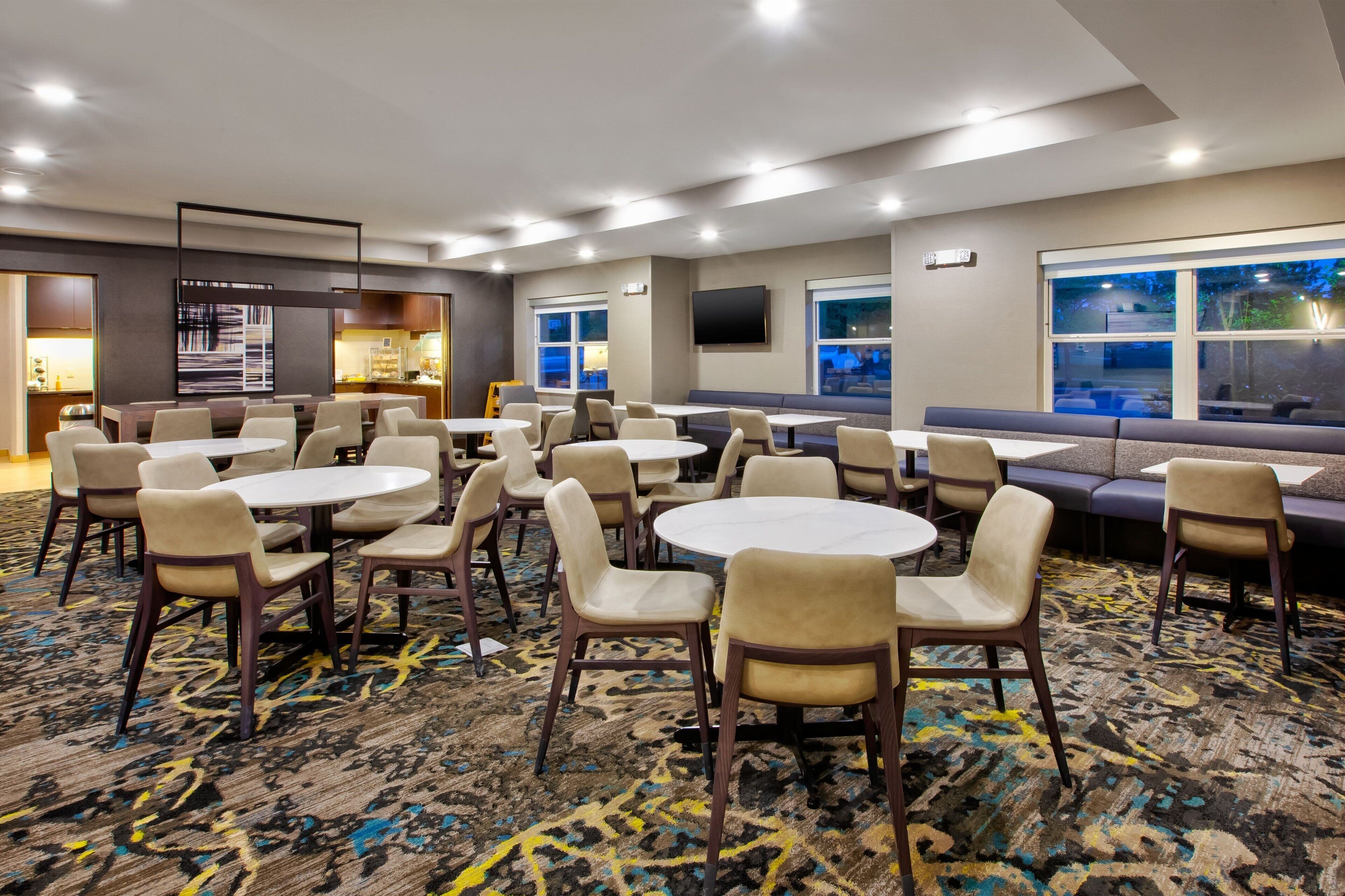 A hotel room with round tables and chairs, a sofa, and a TV mounted on the wall.