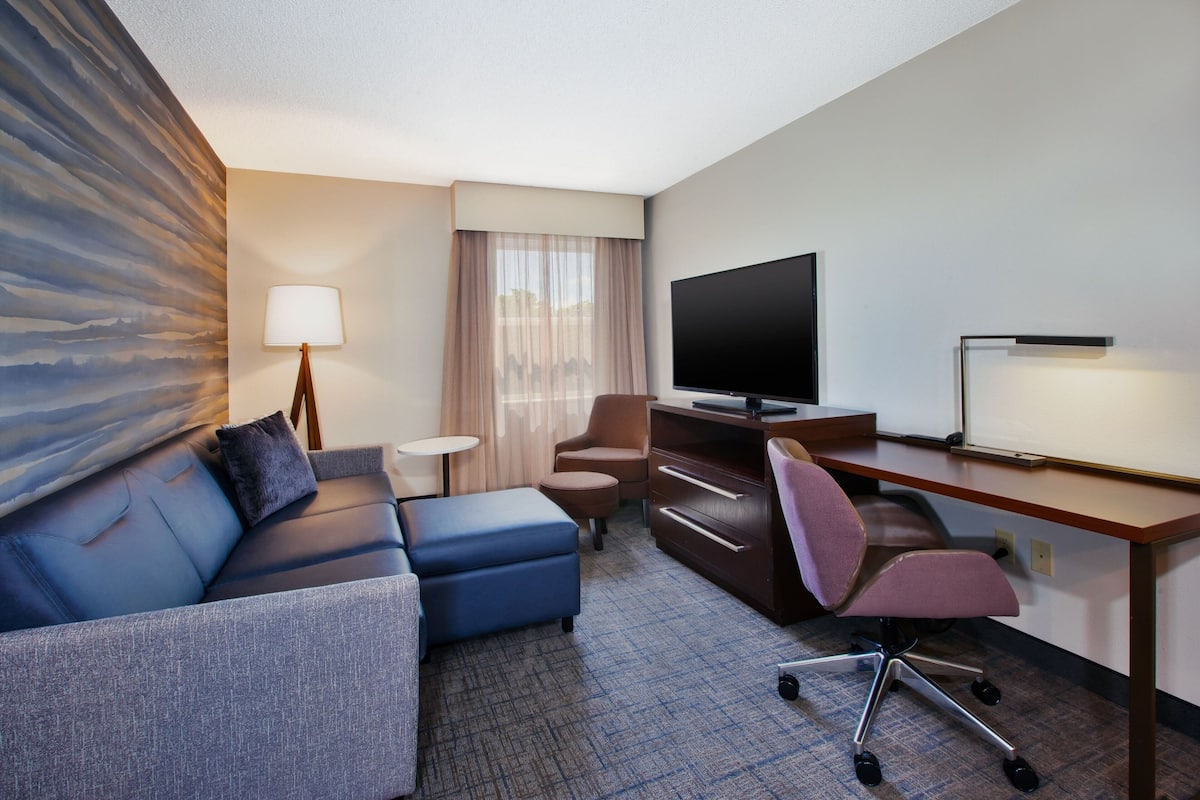 A hotel room with a sofa, a desk, a TV, and a lamp.
