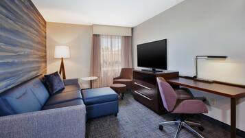 A hotel room with a sofa, a desk, a TV, and a lamp.